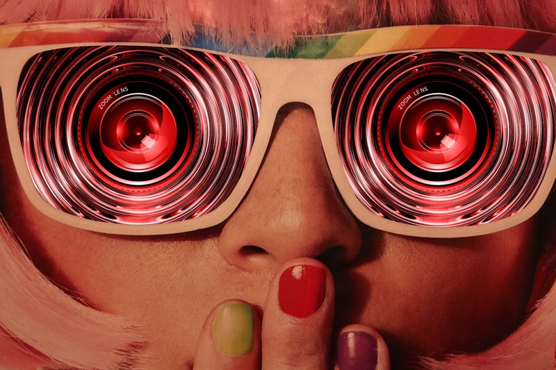 foto artistica di donna bionda su sfondo arancione con mani alla bocca e unghie colorate che indossa occhiali con lenti concentriche colorati al loro interno obiettivo fotografico, zoom lens